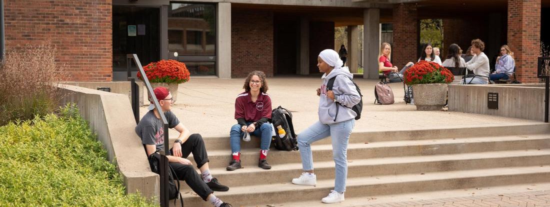 Three Hamline students gathered on a set of outdoor stairs on campus