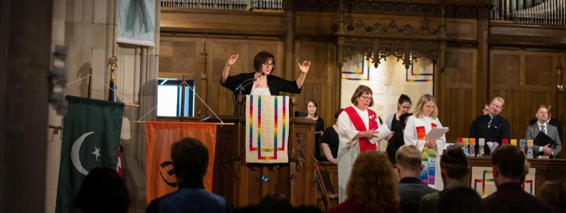 A person speaking at a podium in the Hamline church with people throughout the room