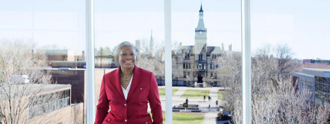 President Fayneese Miller standing in front of a window with Old Main in the background