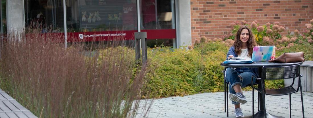 Hamline student sitting at outside table on campus doing schoolwork