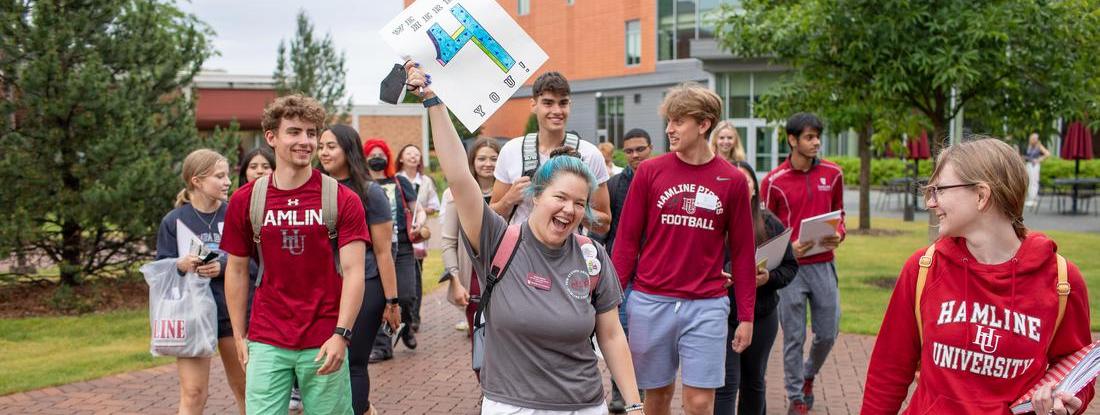 Hamline happy  students waliking toghther holding a four sign 