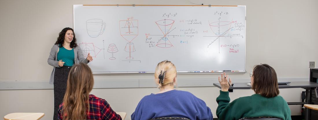 Photo of students in a classroom with the professor at the whiteboard