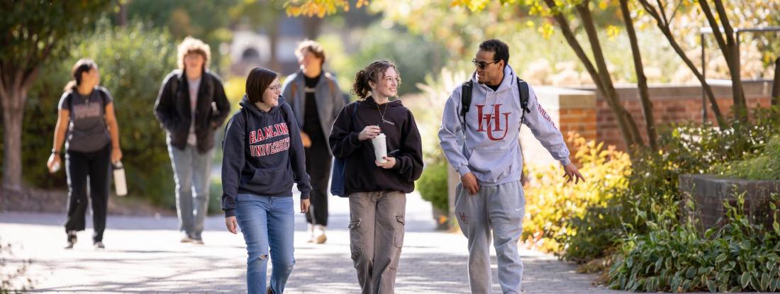 Three students with Hamline sweatshirts walking on campus in fall