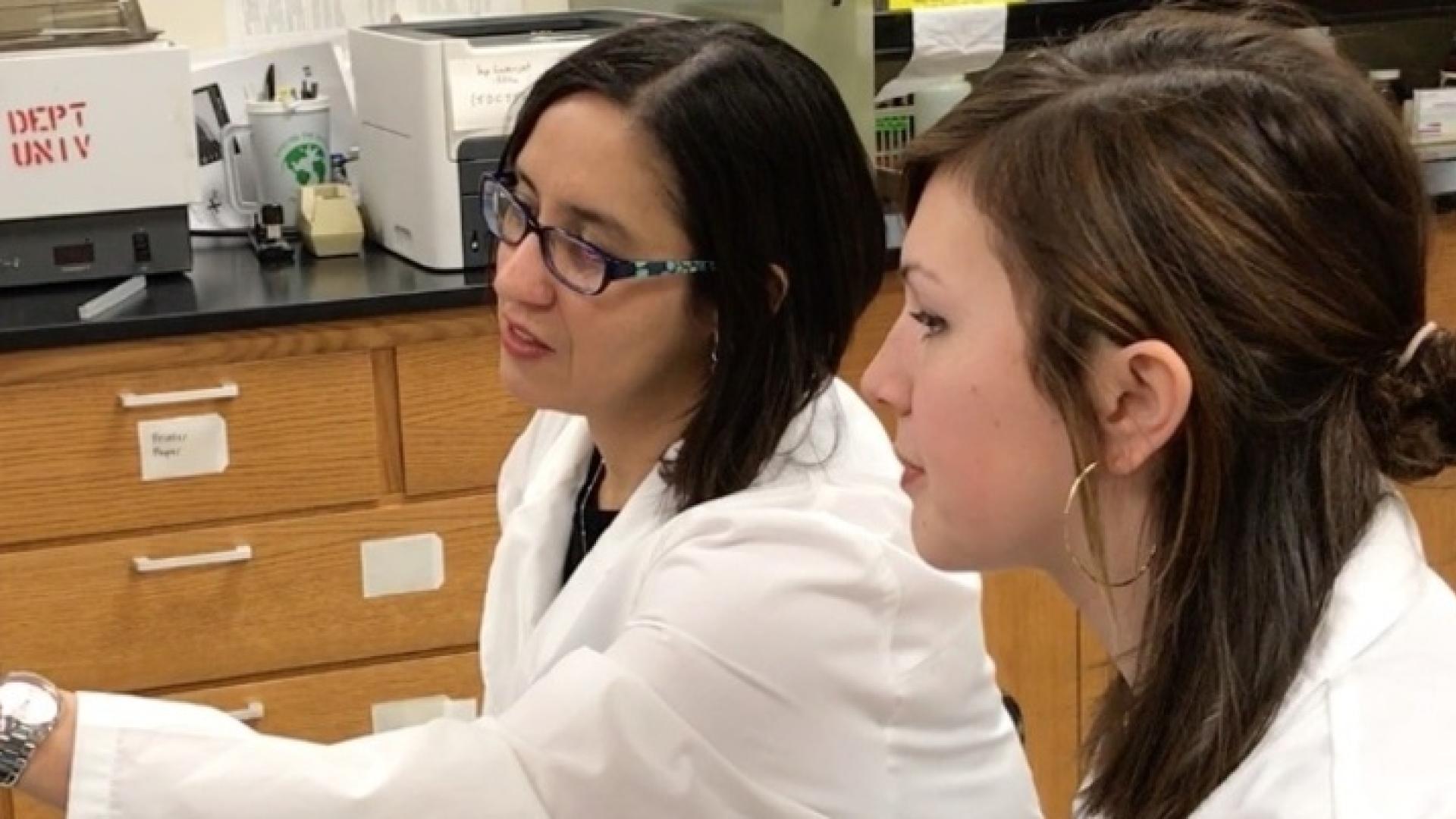 Two Hamline biology students in white coats looking at an image on a computer together