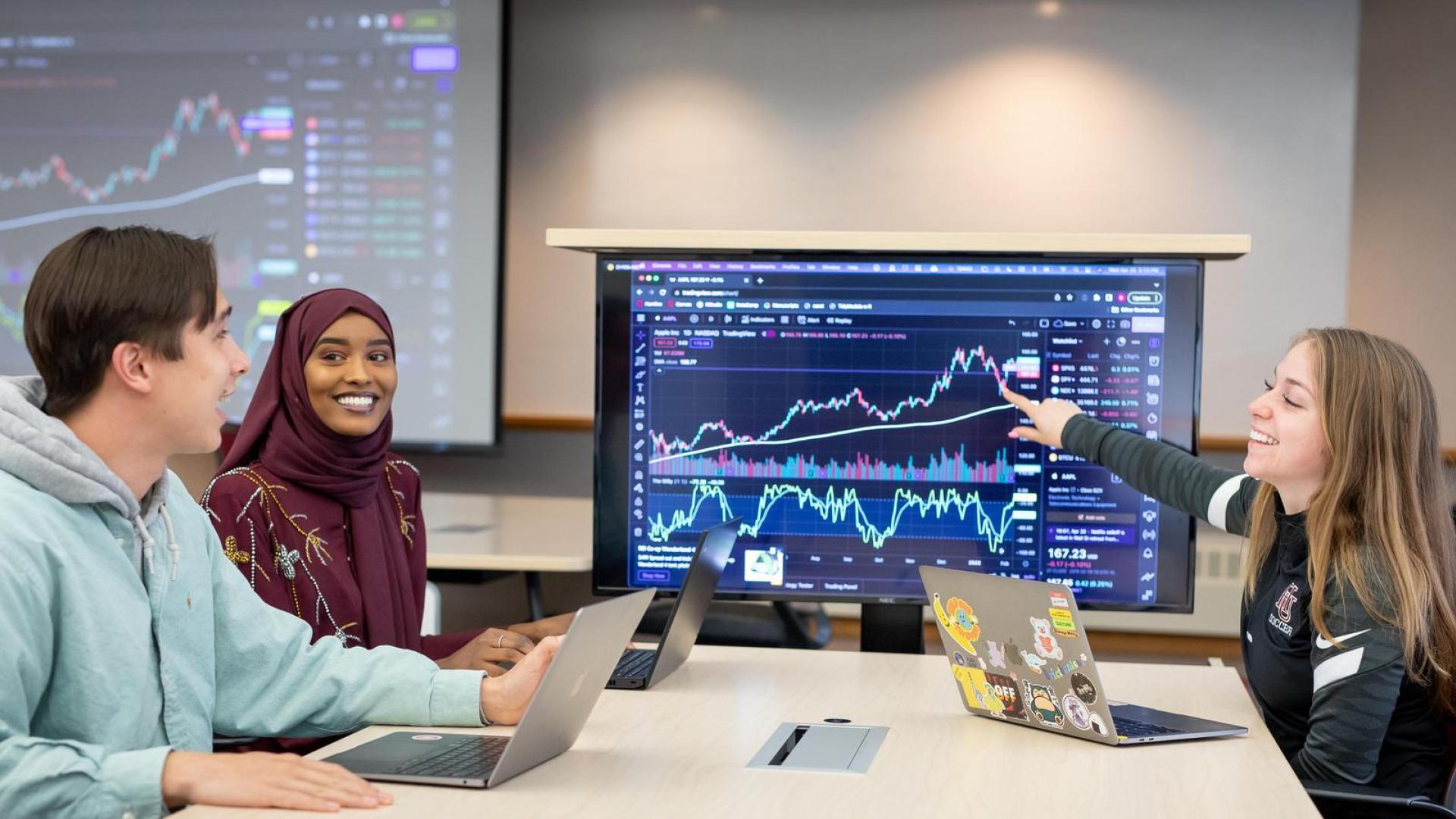 Three students working at a table in front of a monitor with data graphs displayed