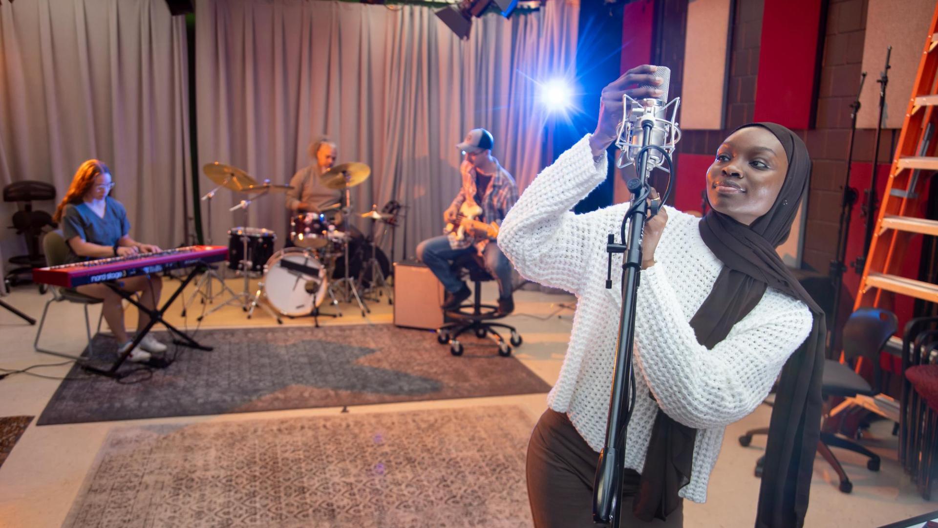 Music production with Jeff Bailey at Hamline University, student adjusting microphone with band in background