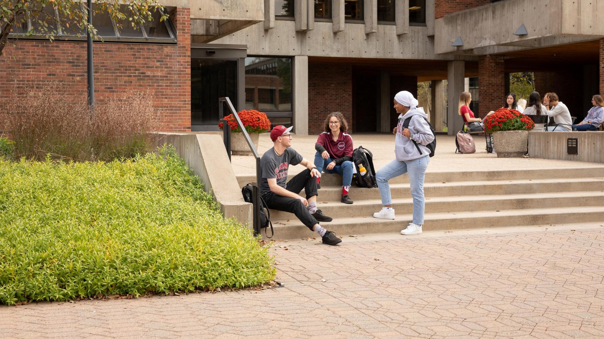 Three Hamline students siting on steps in front of Bush Library