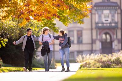 Three students walking in front of Old Main in fall