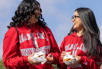 Two students carrying food and laughing during Hamline Homecoming and Alumni Weekend