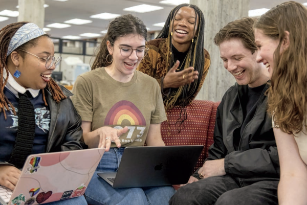 Group of students laughing while looking at laptops in the library